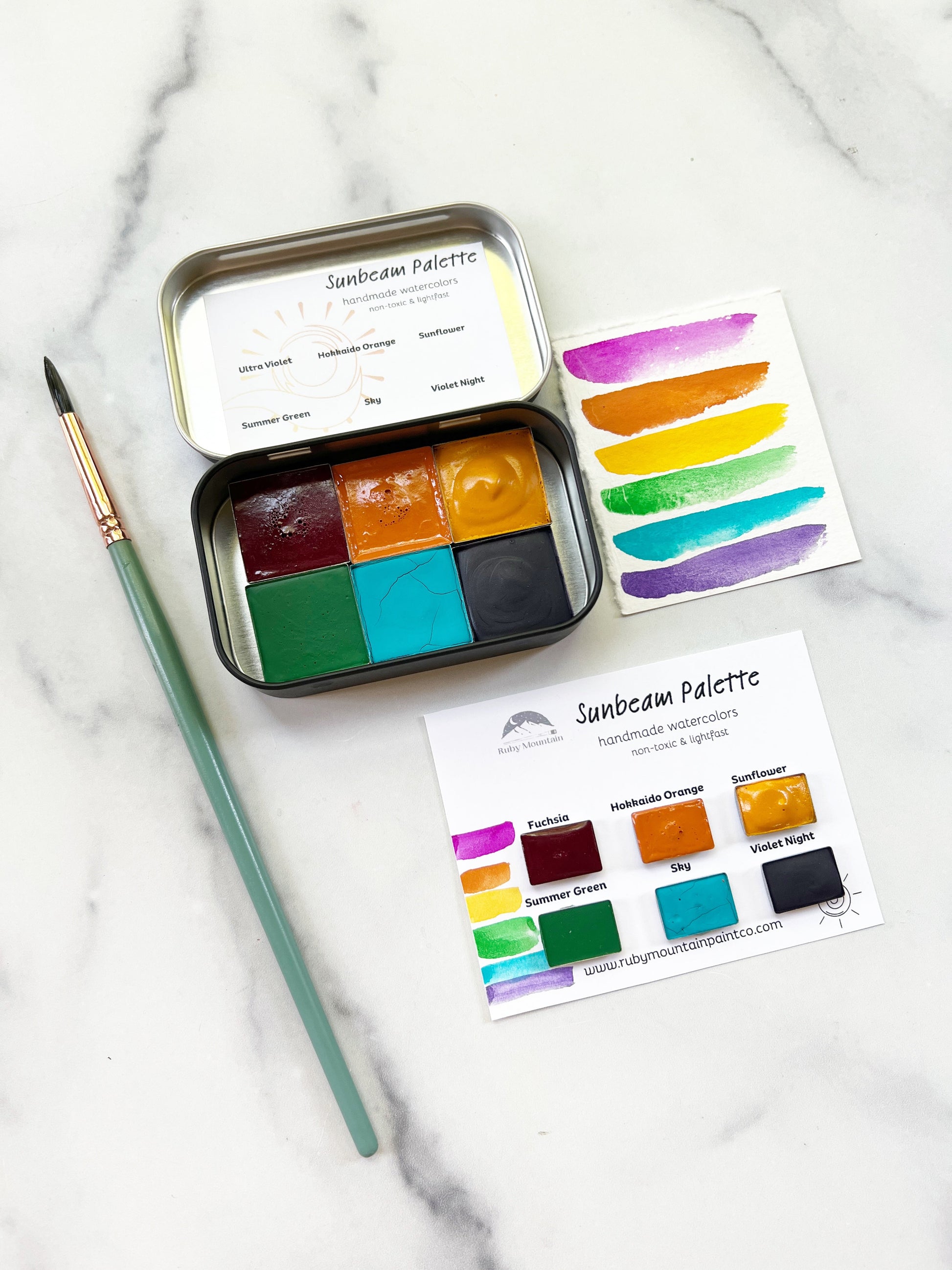 Set of watercolor paints in a tin with color swatches on a marble surface