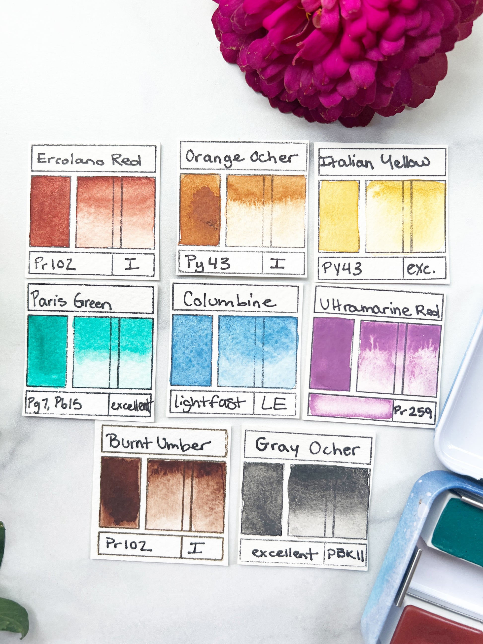 Color swatch chart with watercolor paint names and a pink flower on a white background