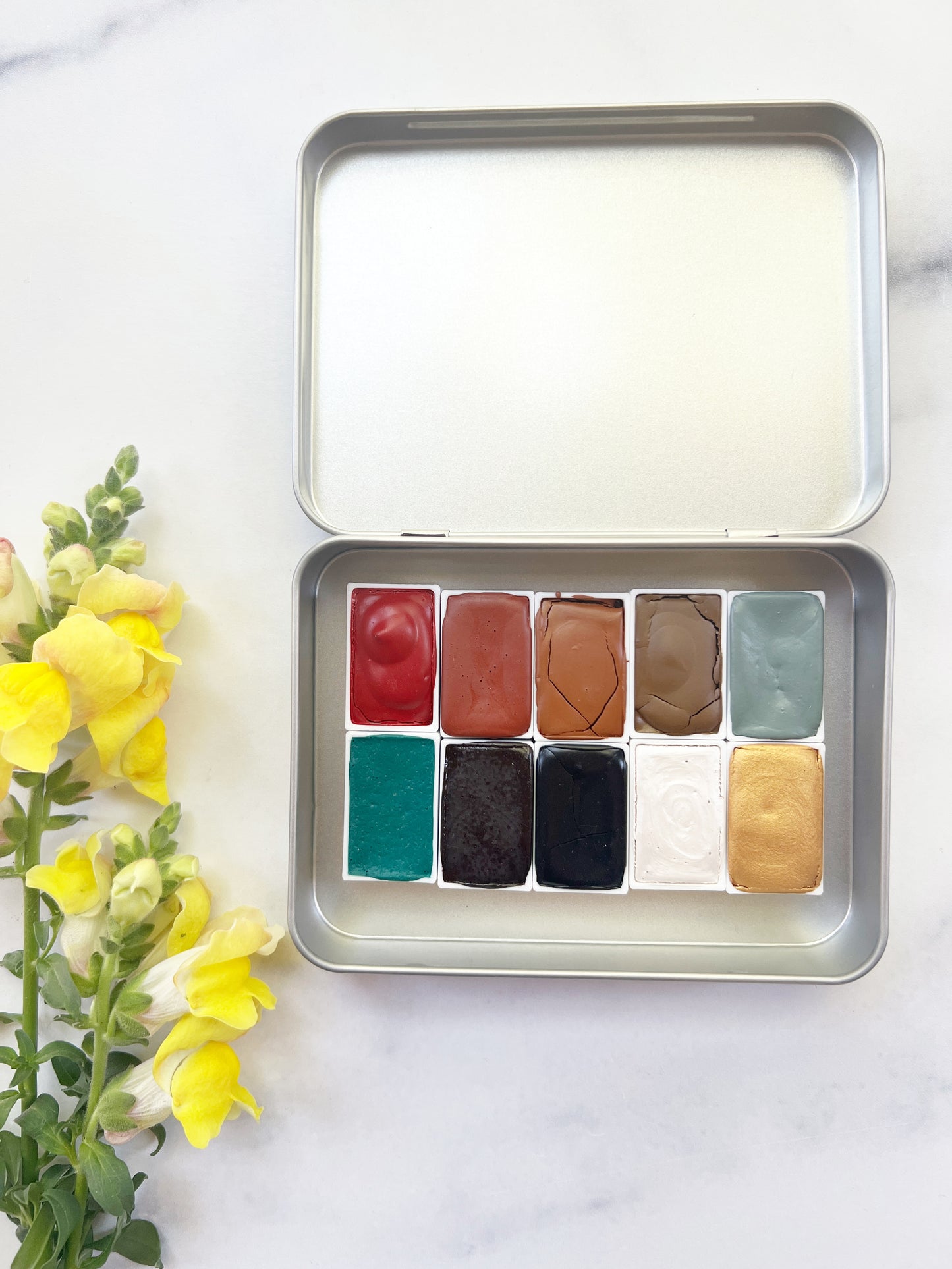 Set of watercolor paints in a metal tin with flowers on a white background